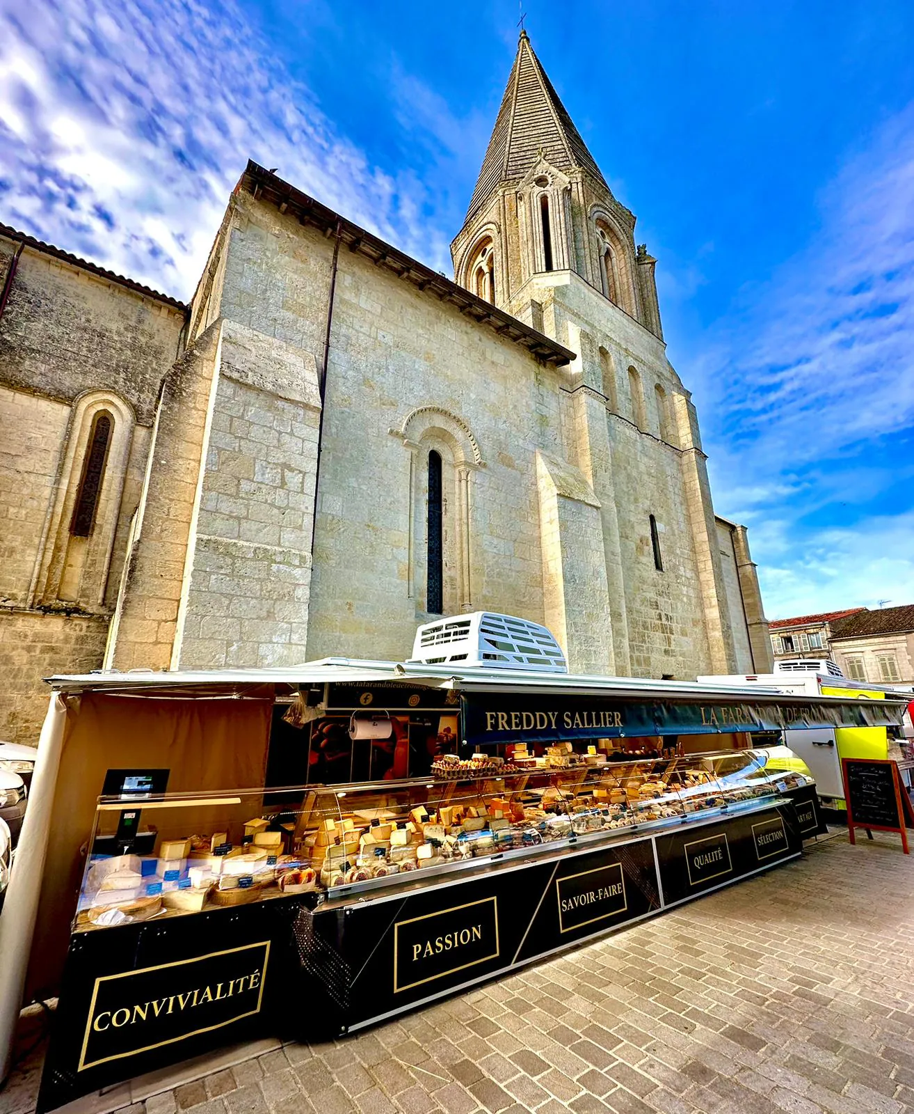 La vitrine réfrigérée du stand de La Farandole de Fromages au pied d'une église